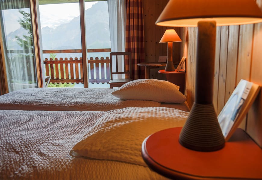 resort in the mountains two beds lamps and wood walls with a view out the sliding glass door of the mountains